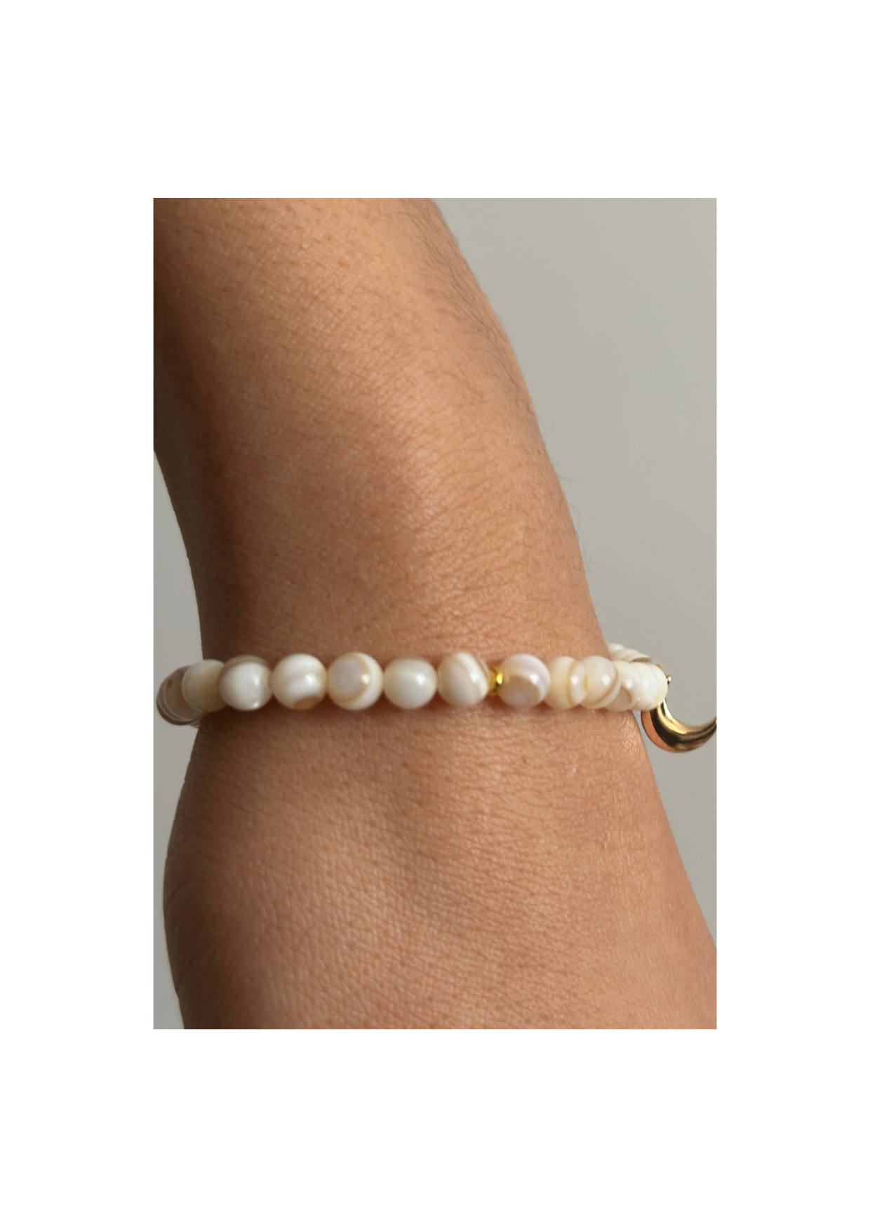 Bracelet tasbih en perles nacrées blanches avec pendentif lune dorée, suspendu au-dessus de sable doré