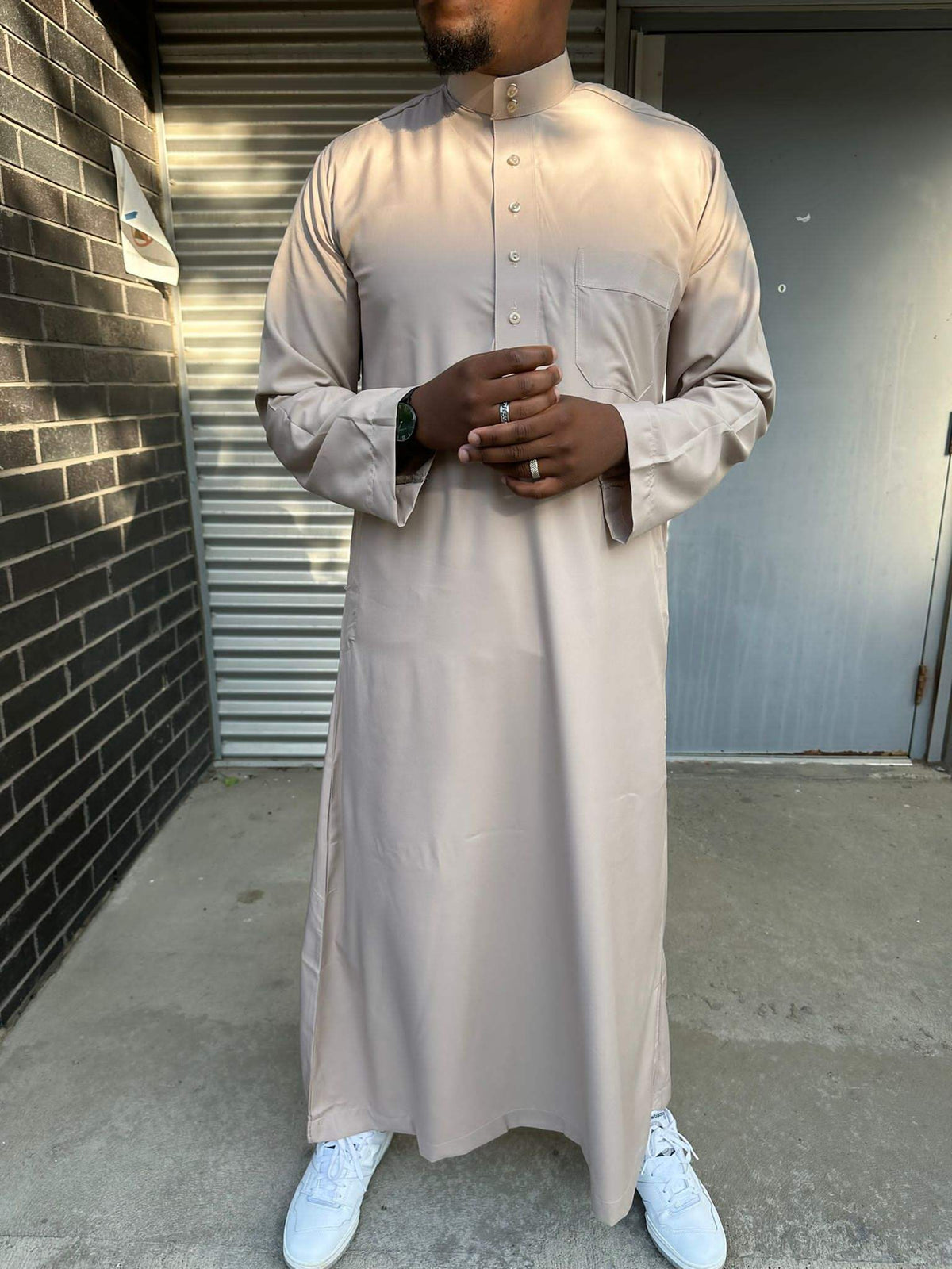  Homme portant un qamis saoudien couleur sable à manches longues, col officier boutonné et poche poitrine, pour un style raffiné et moderne.