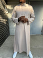  Homme portant un qamis saoudien couleur sable à manches longues, col officier boutonné et poche poitrine, pour un style raffiné et moderne.