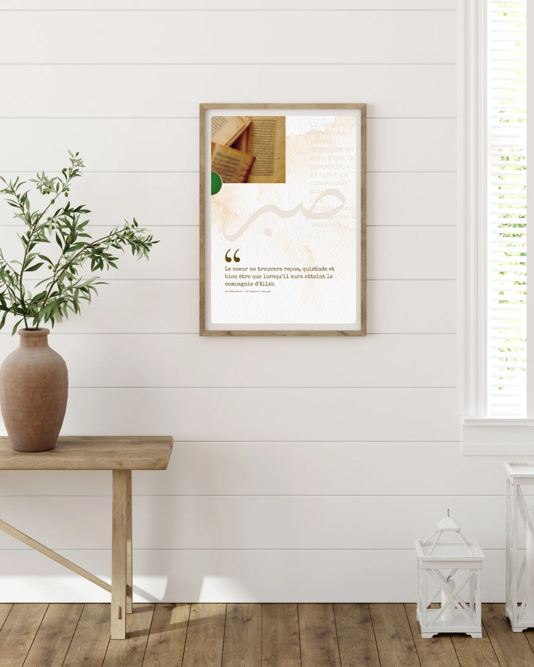 Affiche murale encadrée en bois avec citation islamique en français, accrochée sur un mur blanc lambrissé, accompagnée d’une table en bois avec vase et d’éléments décoratifs lumineux au sol.
