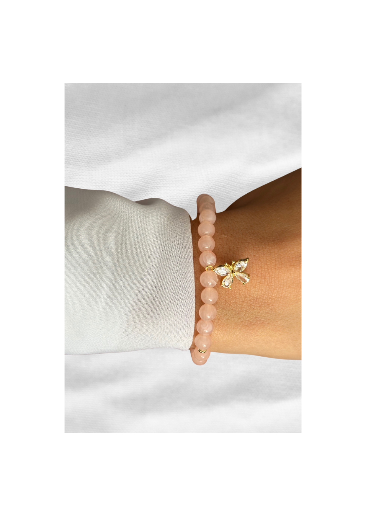 Bracelet artisanal en perles de quartz rose avec un pendentif papillon doré porté au poignet