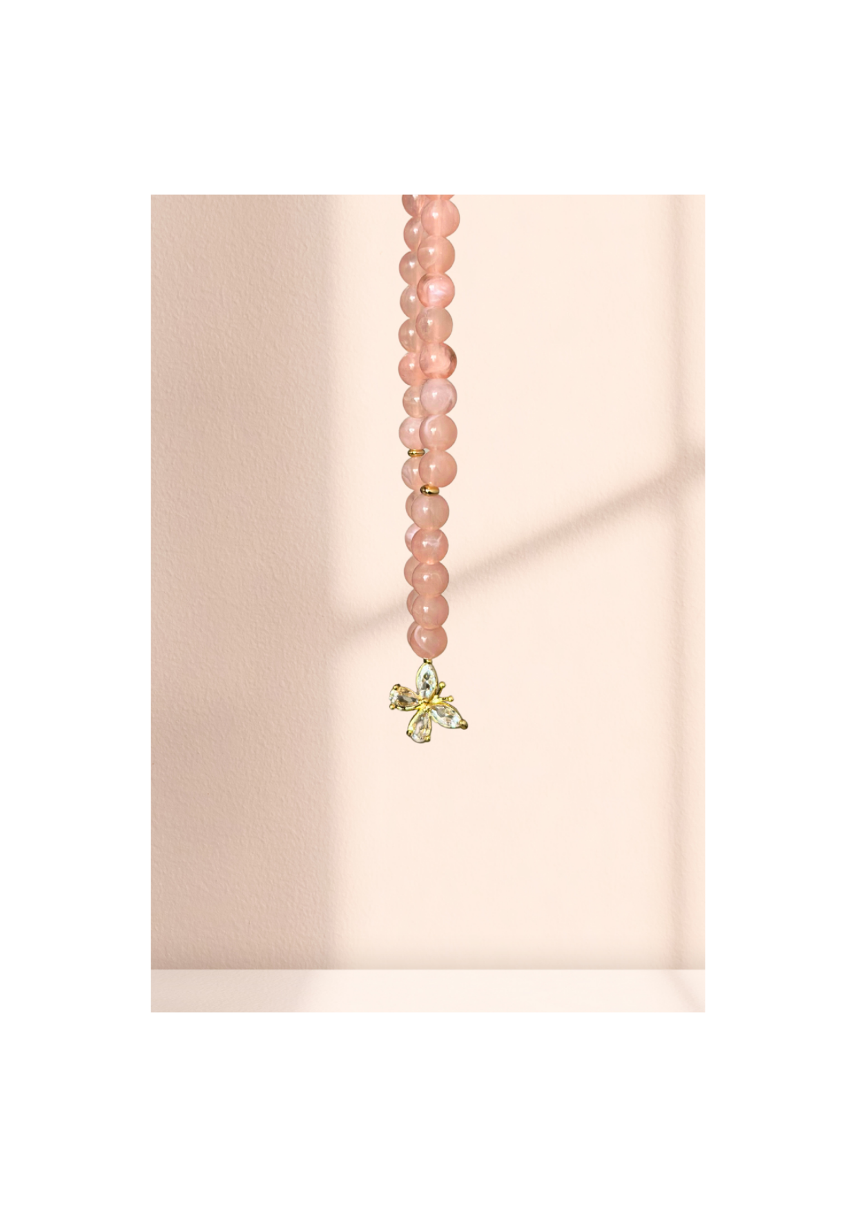 Chapelet élégant en quartz rose avec pendentif papillon doré suspendu sur un fond pastel