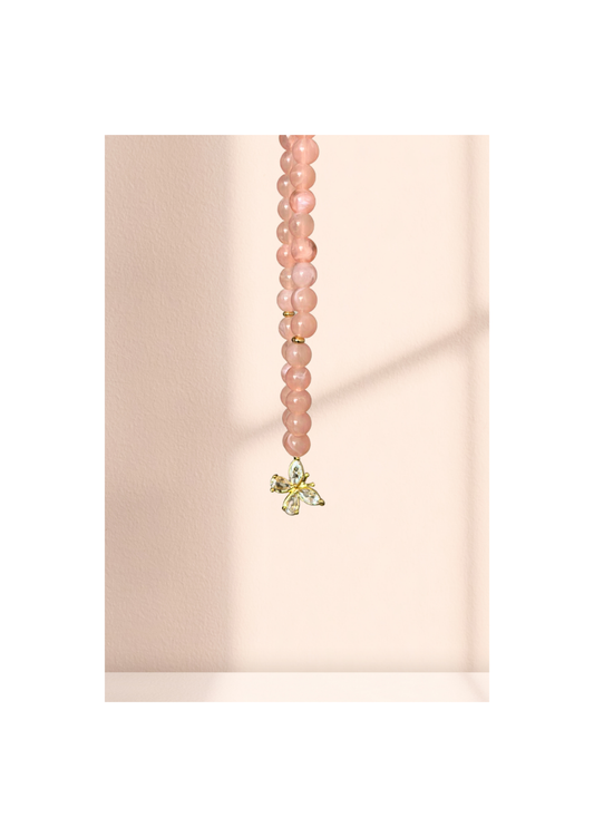 Chapelet élégant en quartz rose avec pendentif papillon doré suspendu sur un fond pastel
