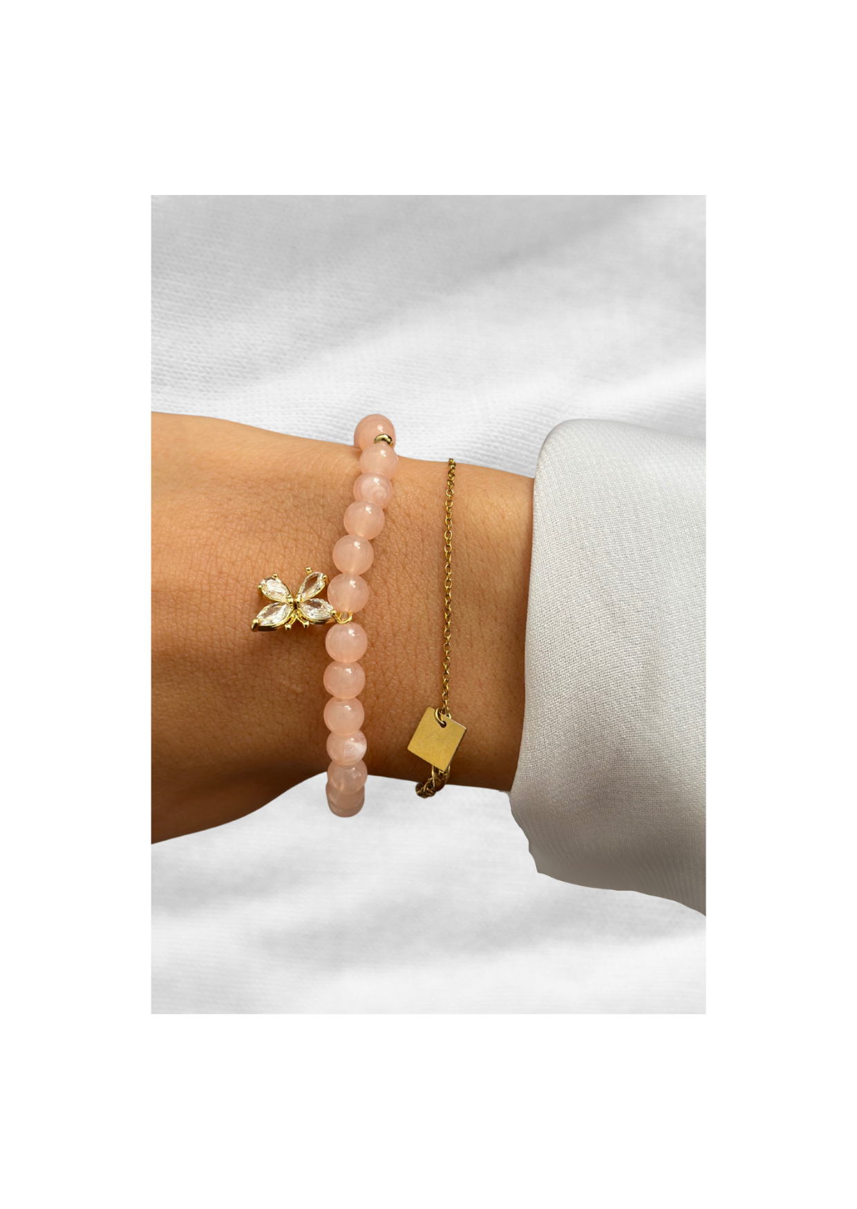 Bracelet en quartz rose avec pendentif papillon doré porté au poignet avec une chaîne fine en or