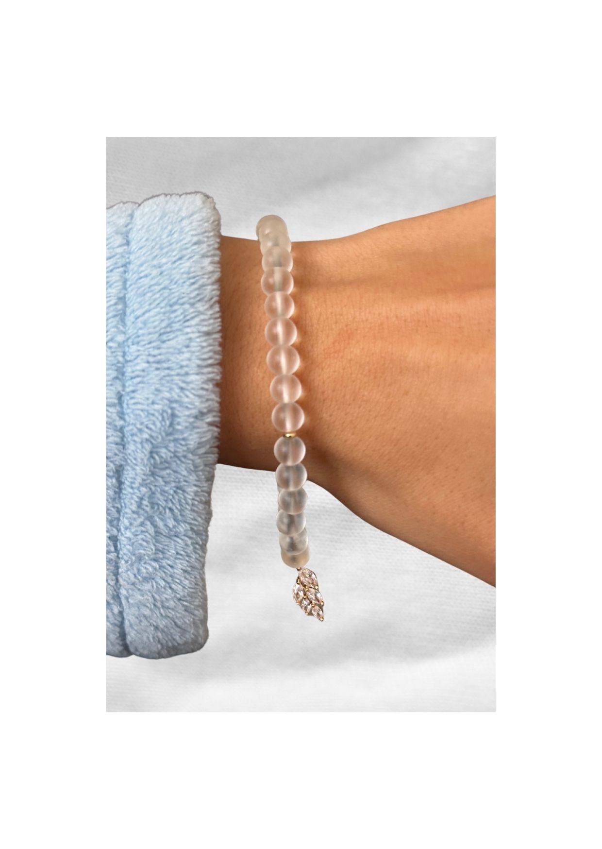 Bracelet tasbih en perles givrées avec pendentif feuille en strass, porté au poignet sur fond clair