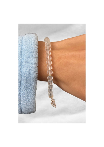 Bracelet tasbih en perles givrées avec pendentif feuille en strass, porté au poignet sur fond clair