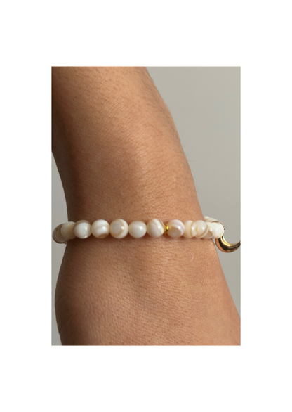 Bracelet tasbih en perles nacrées blanches avec pendentif lune dorée, suspendu au-dessus de sable doré
