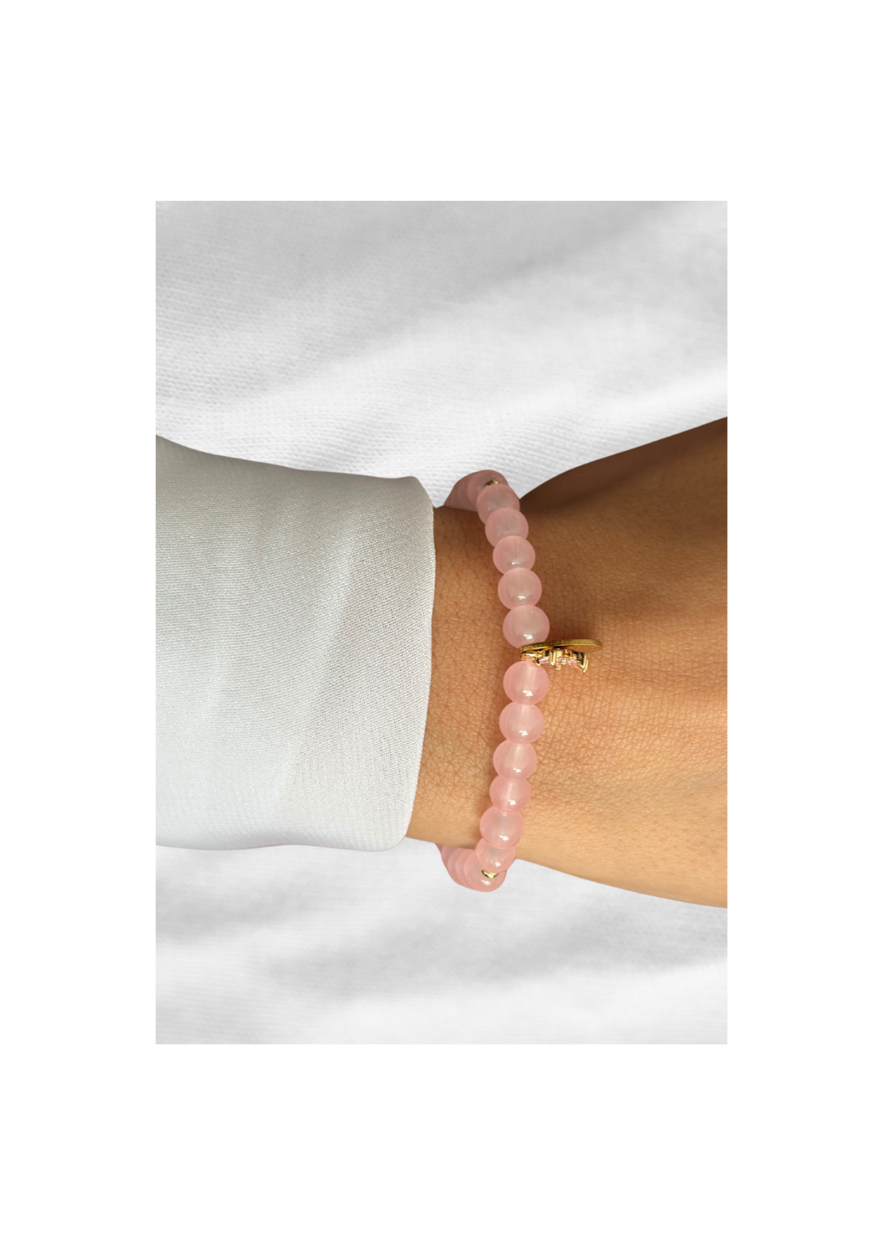 Bracelet tasbih en perles roses avec pendentif doré, porté au poignet sur fond blanc