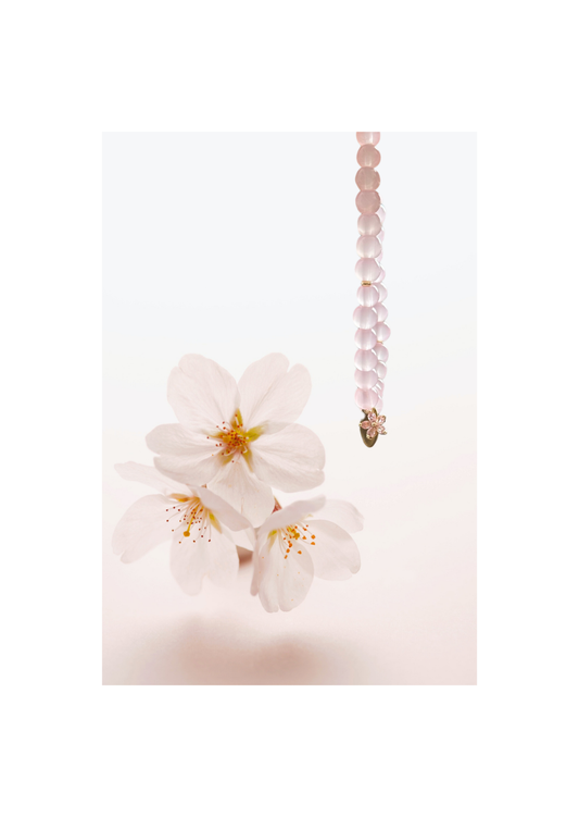 Bracelet tasbih en perles rose pâle avec pendentif en forme de fleur, suspendu à côté de fleurs de cerisier sur fond doux