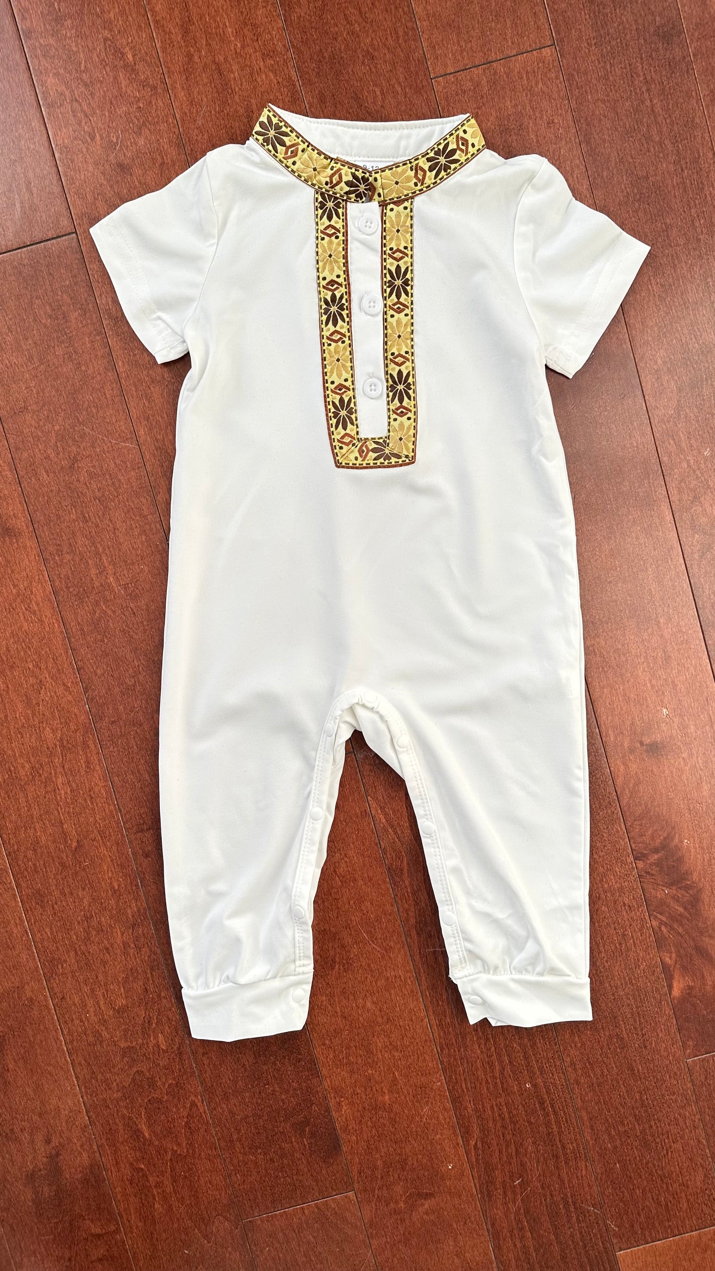 Combinaison blanche pour bébé avec col et patte de boutonnage brodés en doré et marron.

