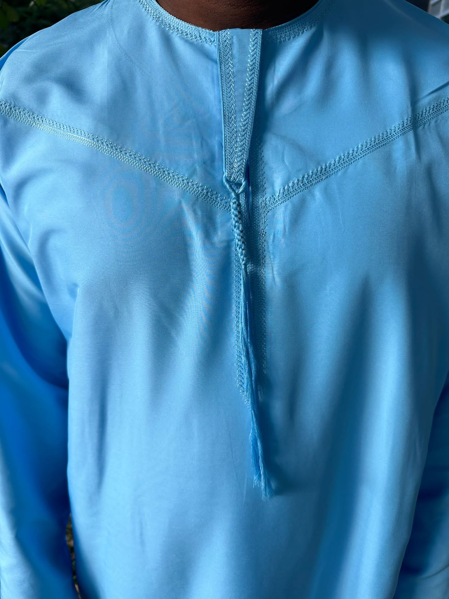 Gros plan sur le col et les coutures décoratives d’un qamis bleu ciel pour homme.