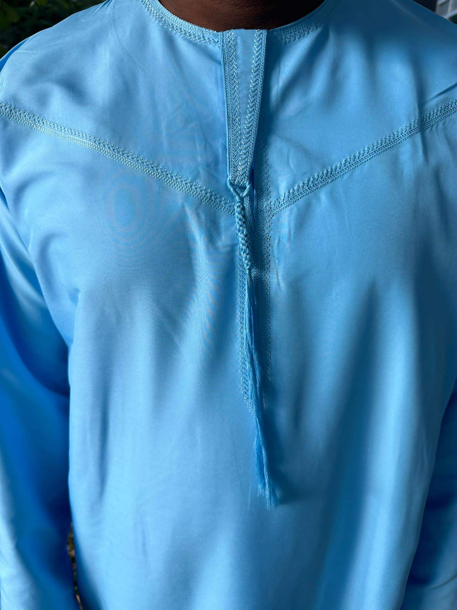 Gros plan sur le col et les coutures décoratives d’un qamis bleu ciel pour homme.