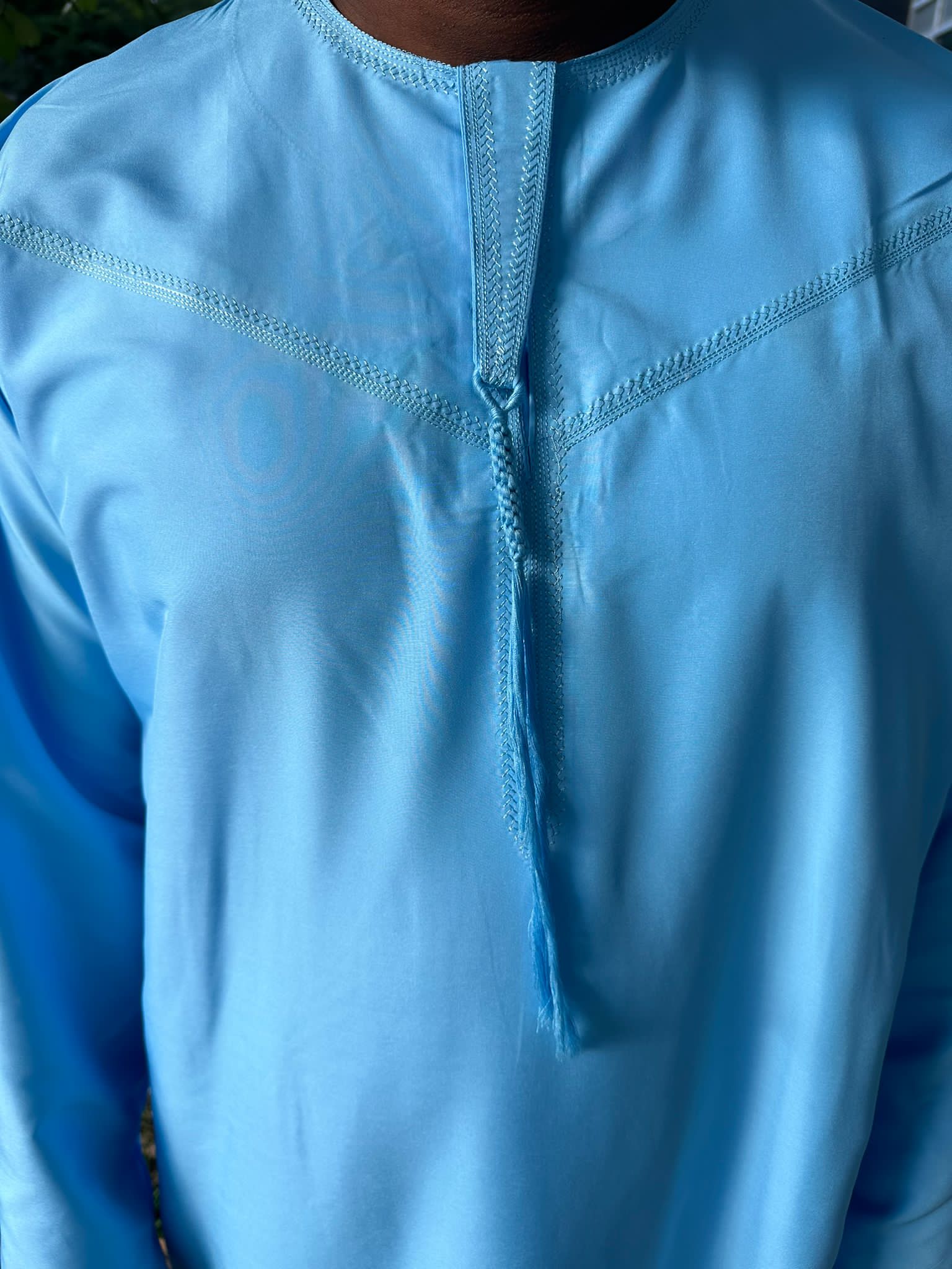 Gros plan sur le col et les coutures décoratives d’un qamis bleu ciel pour homme.