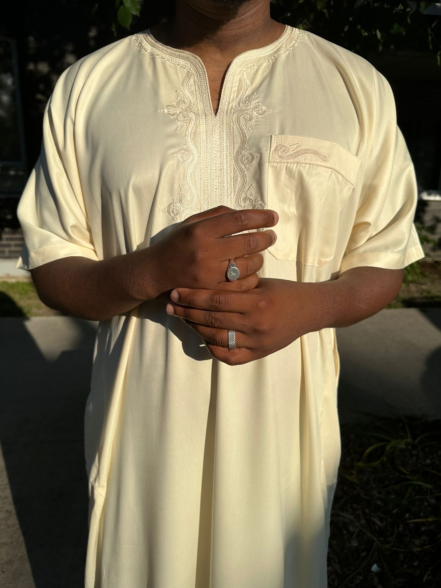 Homme portant une djellaba beige à broderies fines sur le col et poche poitrine, tenue traditionnelle élégante
