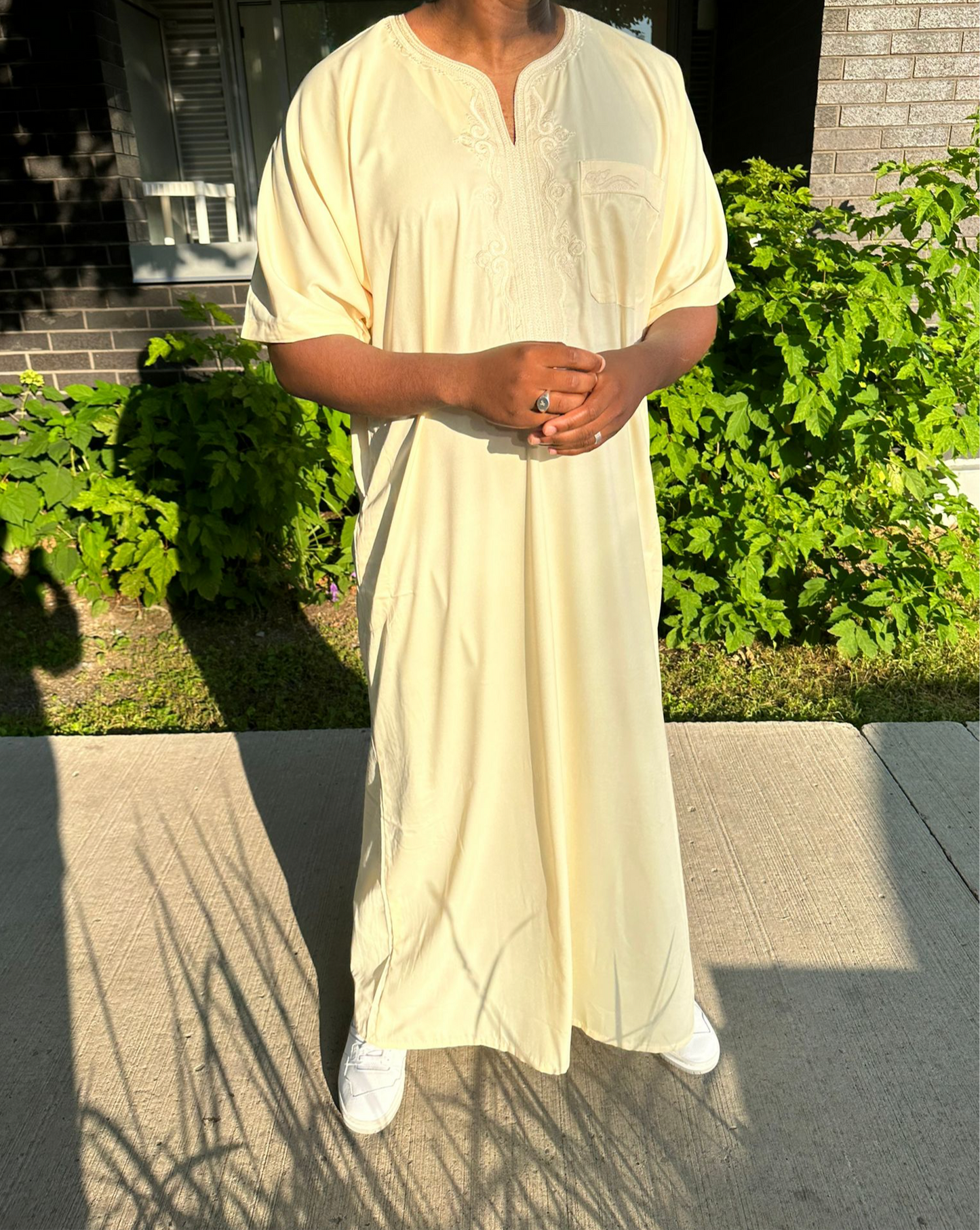 Homme debout portant une djellaba beige longue avec des baskets blanches