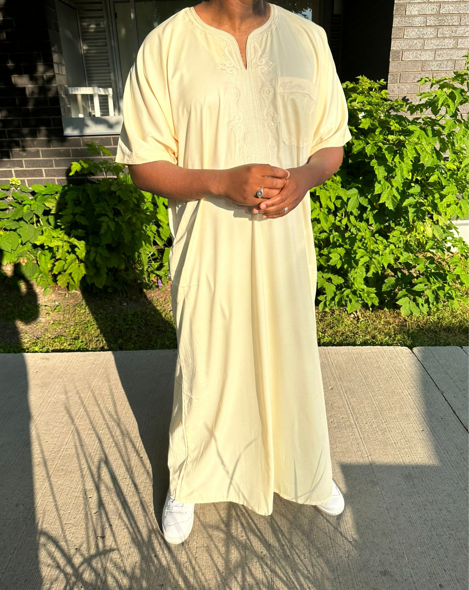Homme debout portant une djellaba beige longue avec des baskets blanches