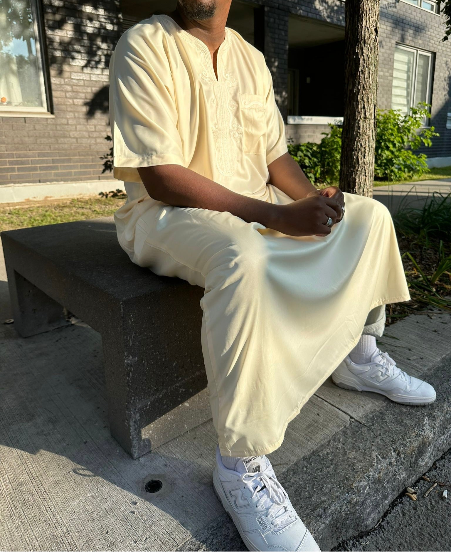 Homme assis portant une djellaba beige traditionnelle avec des baskets blanches

