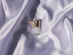 Small perfume bottle with a gold cap placed on light purple silk fabric.