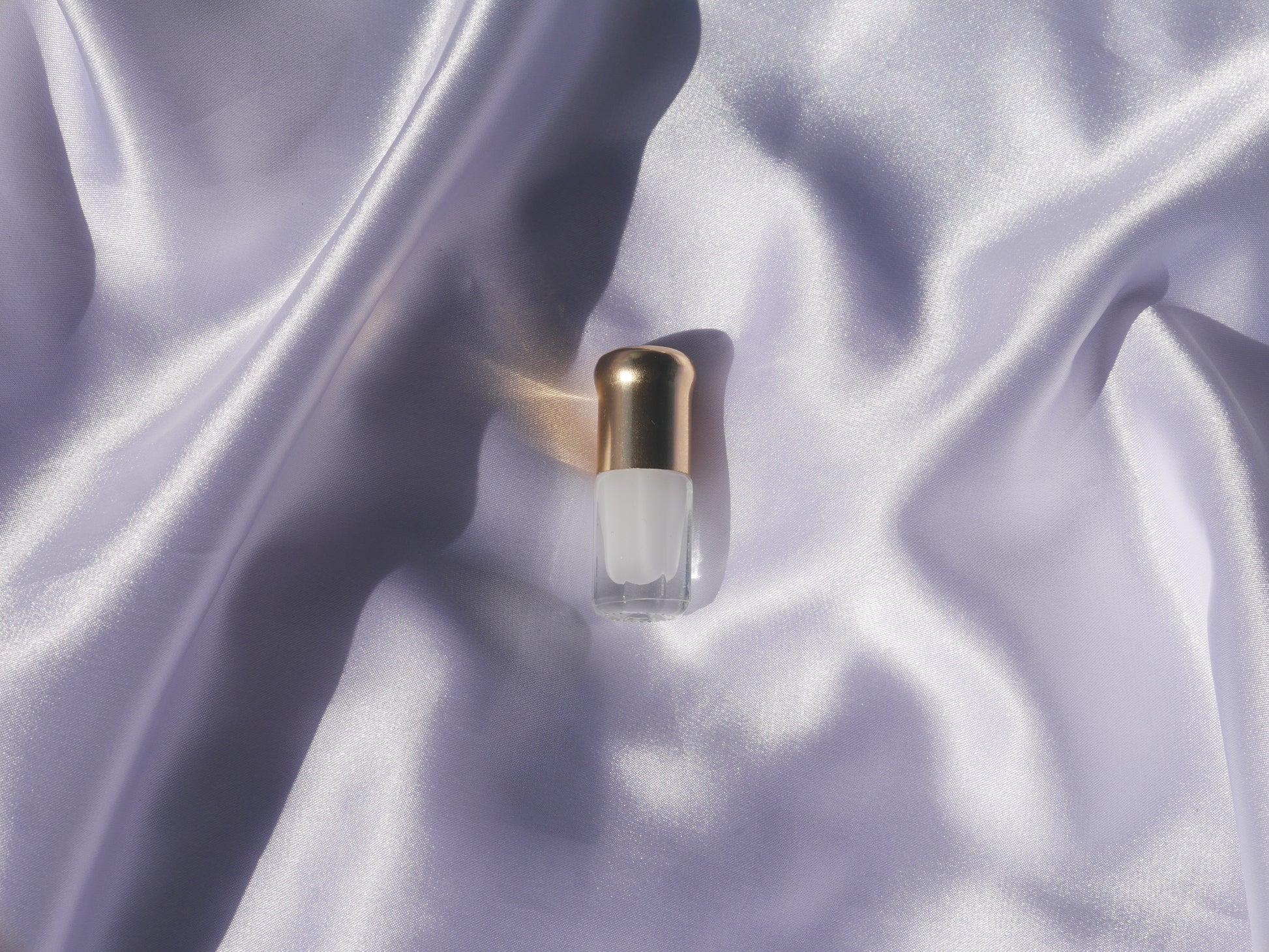Small perfume bottle with a gold cap placed on light purple silk fabric.