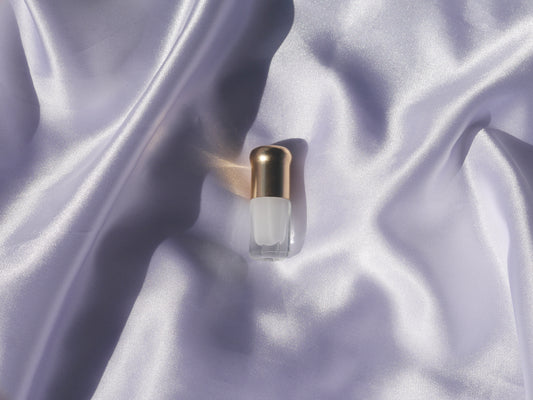Small perfume bottle with a gold cap placed on light purple silk fabric.