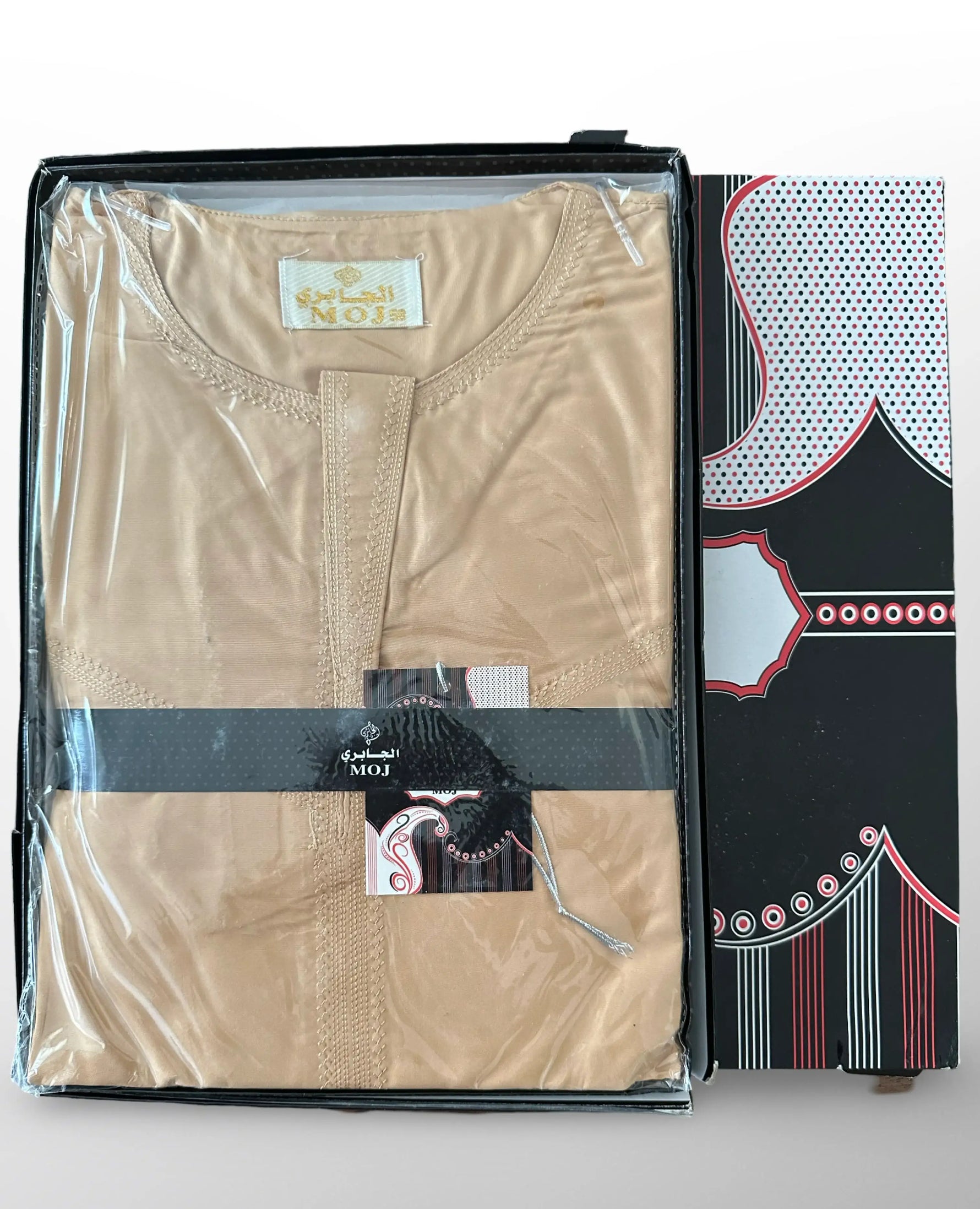 Qamis beige plié dans un emballage transparent avec boîte noire et motifs rouges et blancs, marque MOJ.