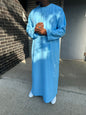  Homme portant un qamis bleu ciel traditionnel, debout avec les mains jointes, en extérieur.