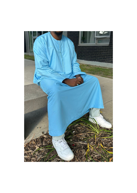  Homme portant un qamis bleu ciel avec des baskets blanches, assis sur un banc en extérieur.
