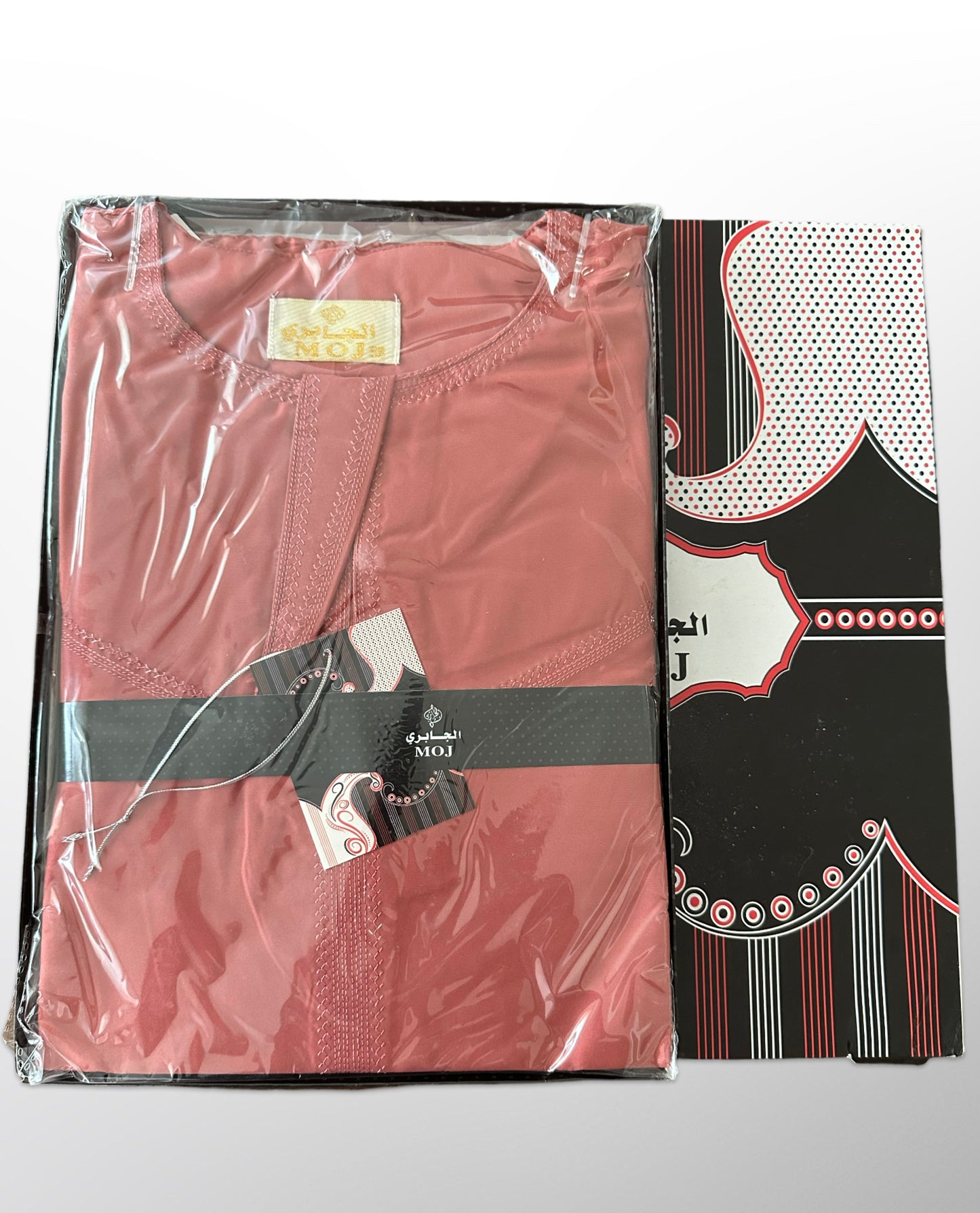 Qamis rouge plié dans un emballage transparent avec boîte noire et motifs rouges et blancs, marque MOJ.

