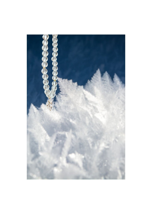 Tasbih en perles blanches givrées avec pendentif feuille en cristal, suspendu devant un fond givré et bleu nuit